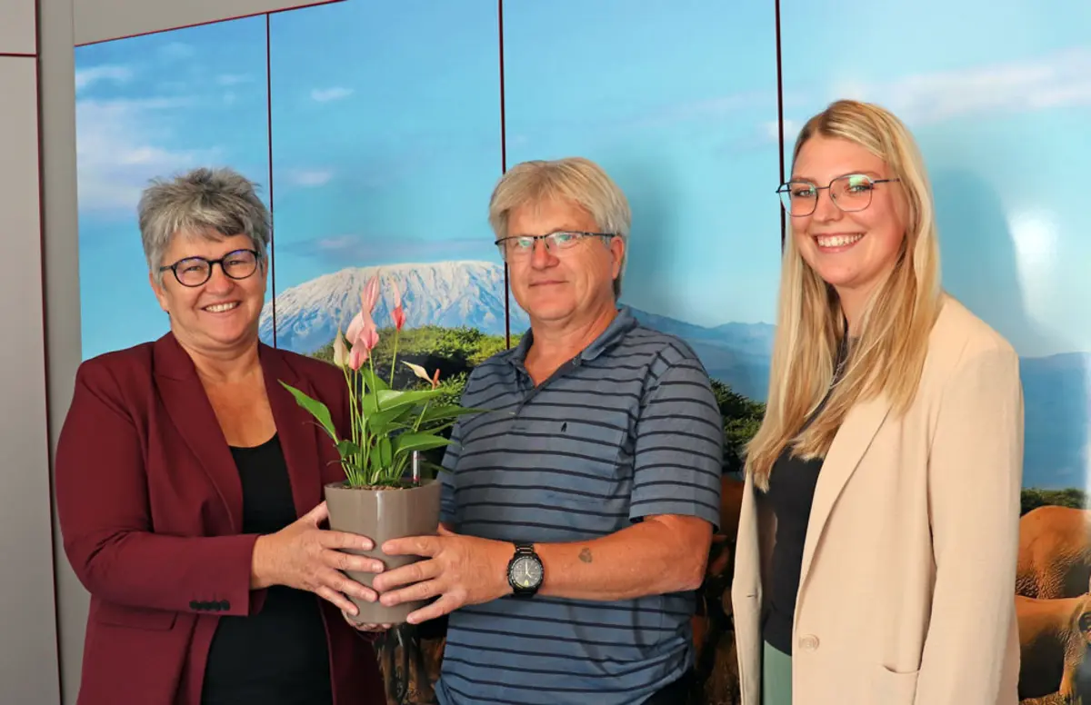 Eine Frau überreicht einem Mann eine Topfpflanze, rechts daneben steht eine junge Frau