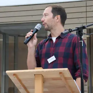 Mann im rotblau karierten Hemd mit Mikrofon in der Hand