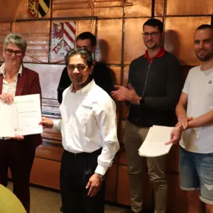 eine Frau und vier Männer vor dem Stadtwappen 