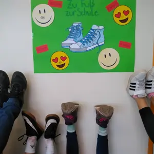 Das Foto zeigt ein Plakat mit symbolischen Schuhen und lachenden Smileys. Darunter strecken Schülerinnen und Schüler ihre Schuhe in das Foto.