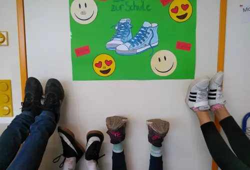 Das Foto zeigt ein Plakat mit symbolischen Schuhen und lachenden Smileys. Darunter strecken Schülerinnen und Schüler ihre Schuhe in das Foto.